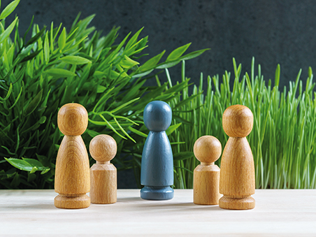 In der Mitte steht eine blaue Spielfigur, rechts und links davon jeweils holzfarbene Spielfiguren, die eine Familie darstellen.