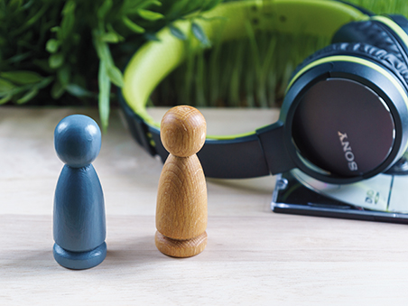 Eine blaue und ein holzfarbene Spielfigur stehen nebeneinander, im Hintergrund liegt ein Kopfhörer.