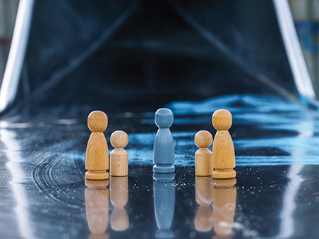 Eine blaue Spielfigur steht in der Mitte, rechts und links davon stehen holzfarbene Spielfiguren, die eine Familie darstellen.