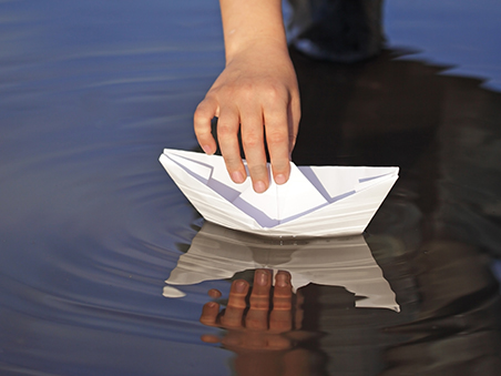 Eine Kinderhand lässt ein Papierboot zu Wasser.