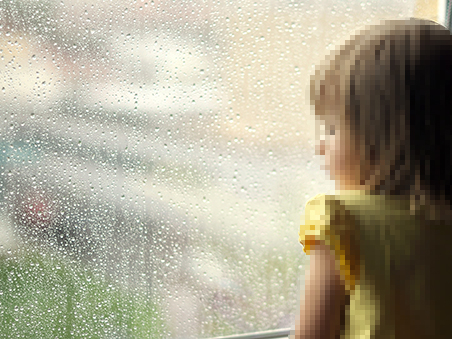 Ein kleines Mädchen schaut traurig aus dem verregneten Fenster.