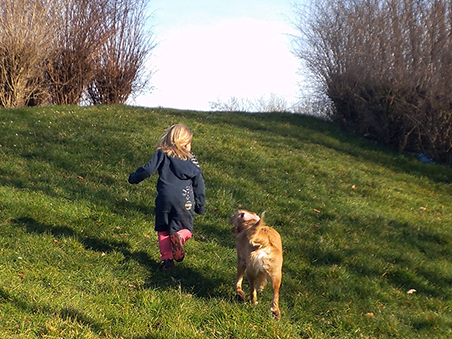 Ein kleines Mädchen läuft gemeinsam mit einem Hund über eine Wiese.
