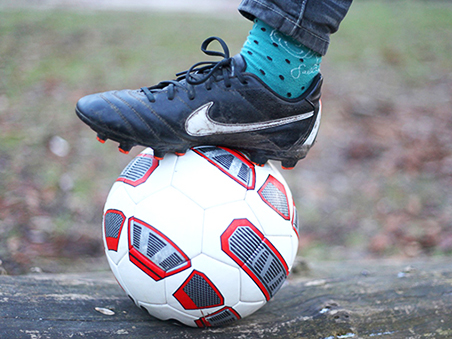 Der Fuß eines Jugendlichen in Fußballschuhen steht auf einem Fußball.