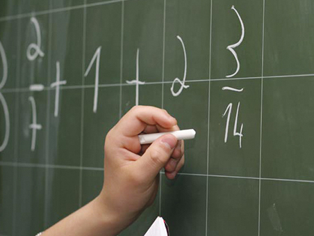 Die Hand eines Erwachsenen schreibt Zahlen an eine Tafel.