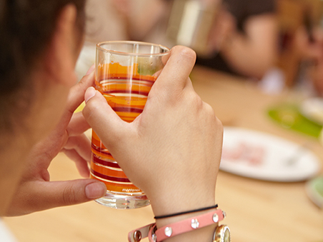 Ein Mädchen sitz mit anderen an einem Tisch und hält ein Glas in der Hand.