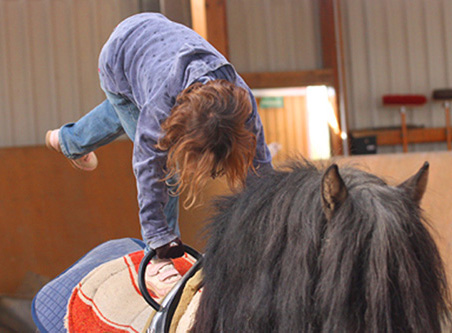Ein Kind turnt auf dem Rücken eines Ponys.