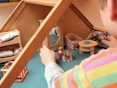 Kind spielt mit einem Puppenhaus im Rahmen der Spieltherapie.